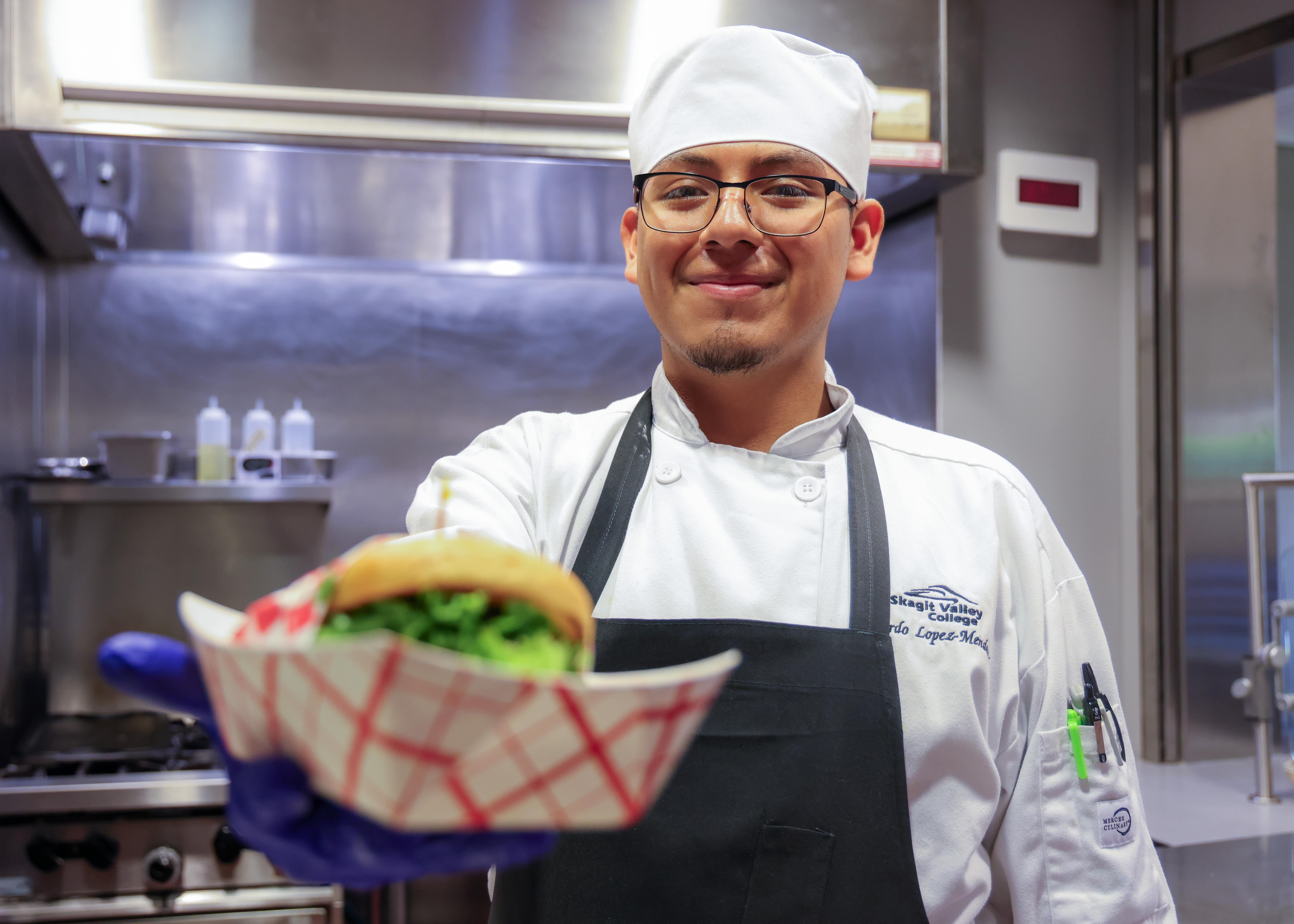 Culinary arts student holding a burger up in front of him