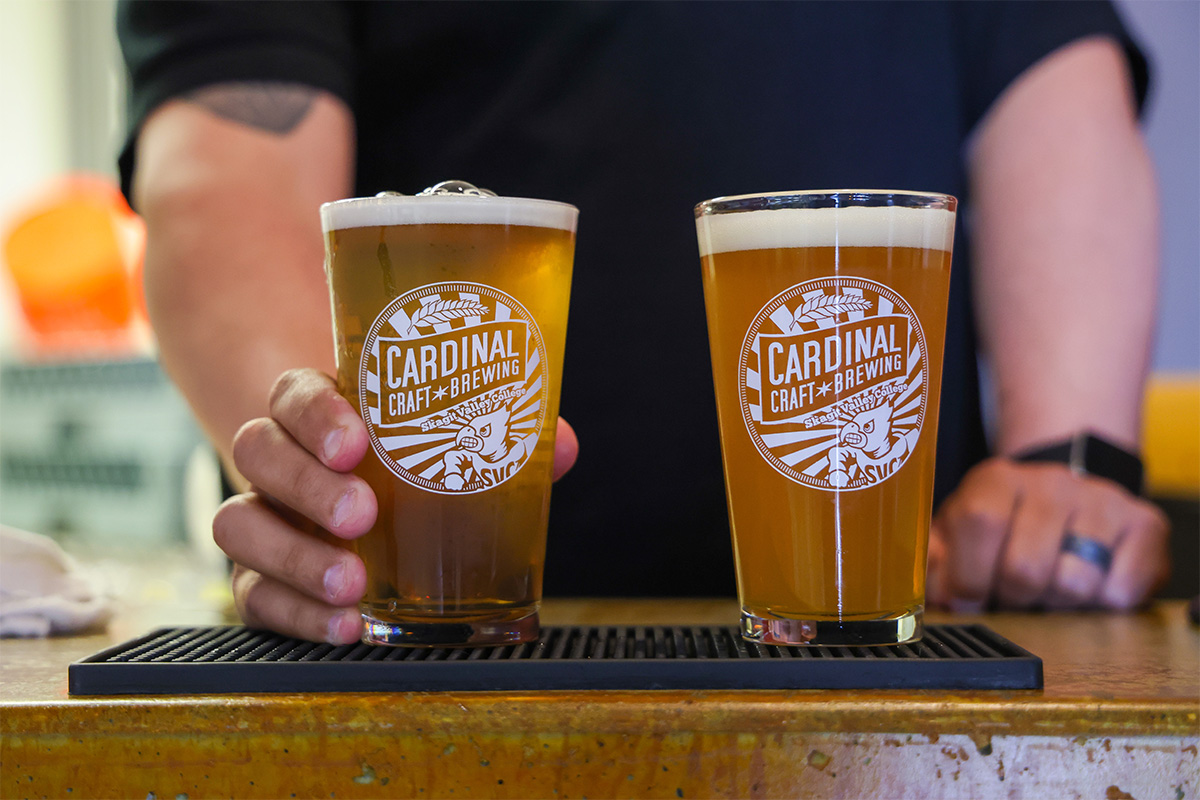 Bartender serving beer in pint glasses that are etched with the cardinal craft brew program's logo